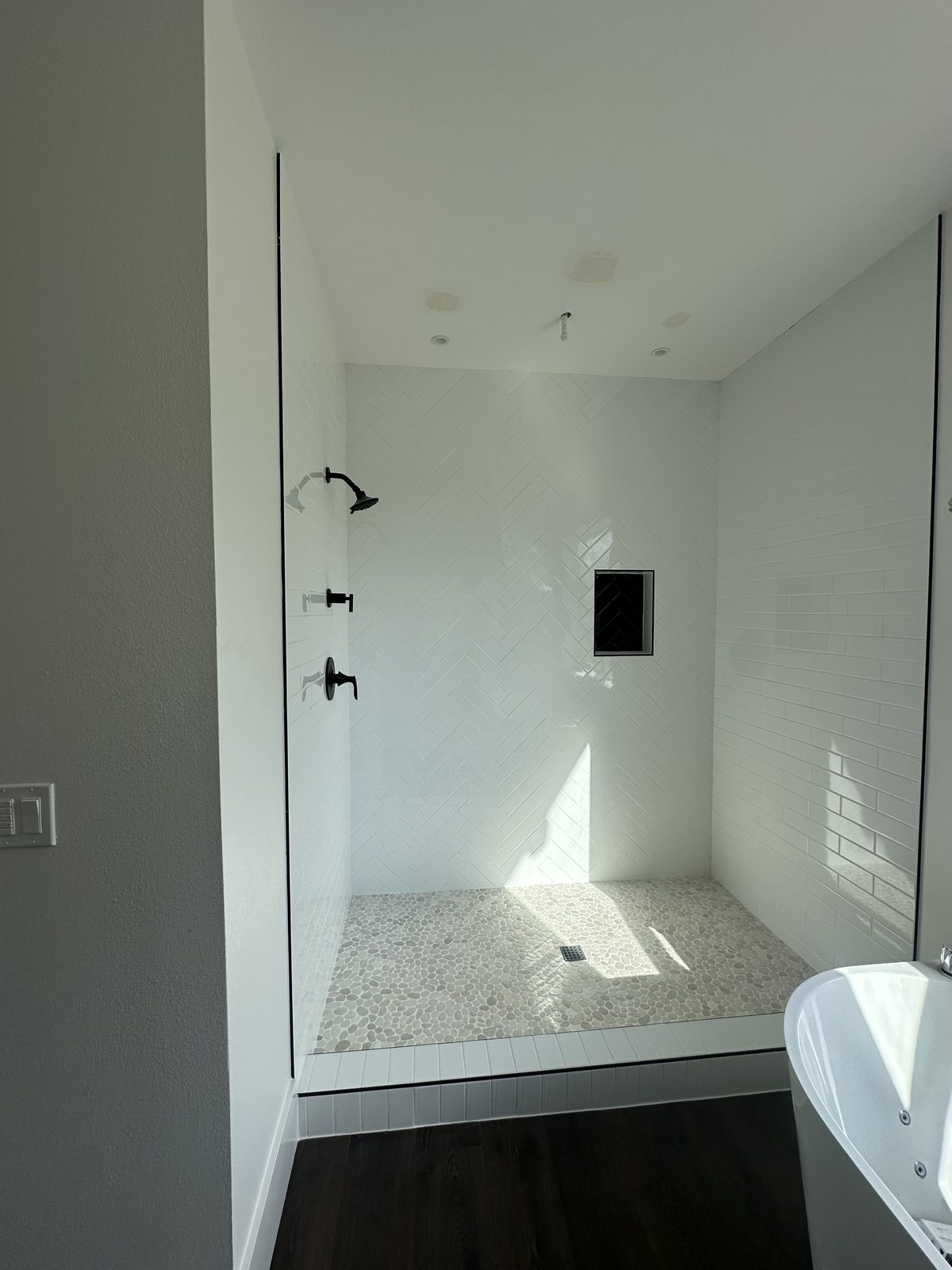 White herringbone tile bathroom showing full shower surround and niche detail, installed by BM Pro Construction