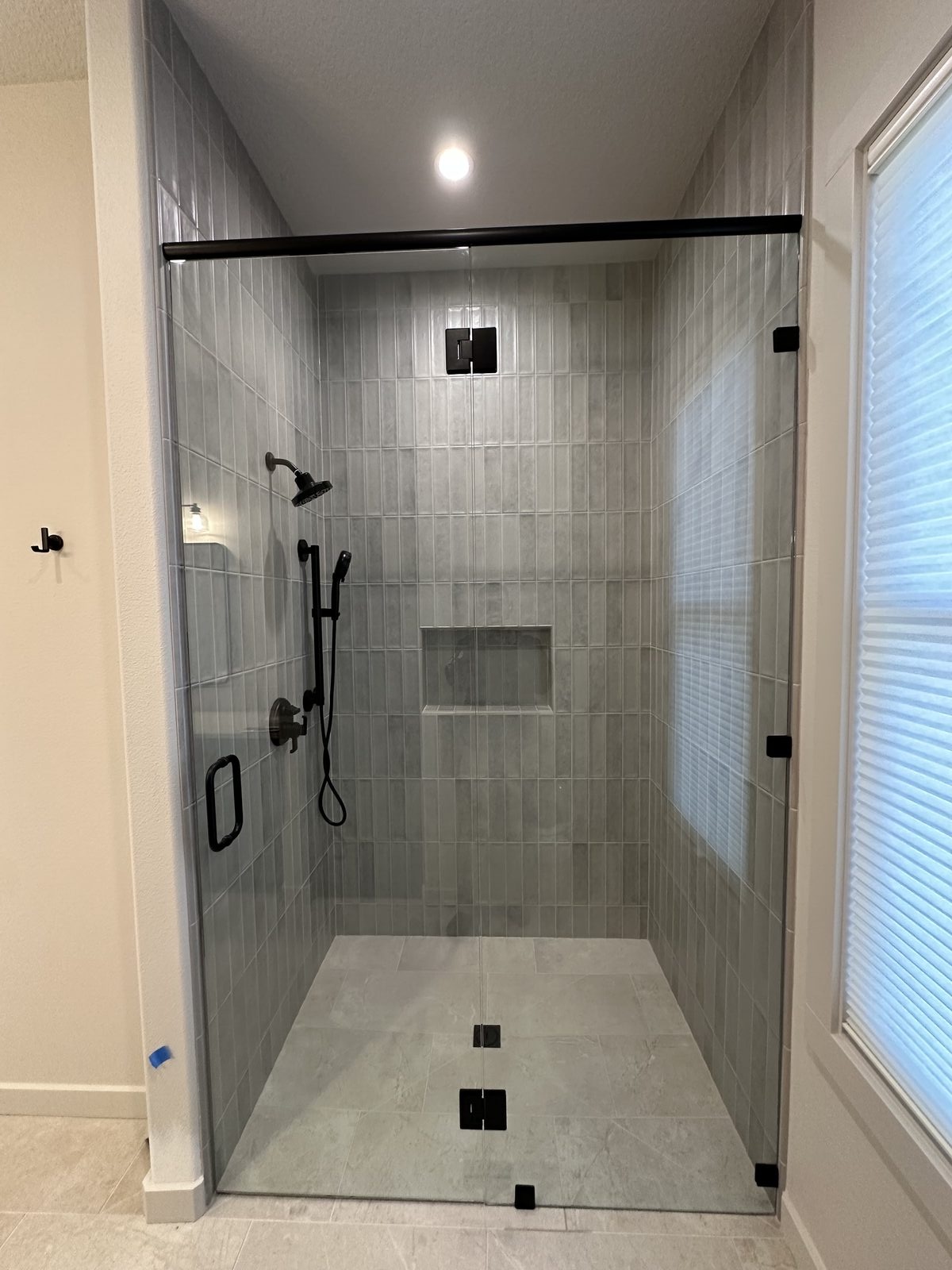 Gray tile shower viewed through the glass enclosure door, showing finished tile work inside